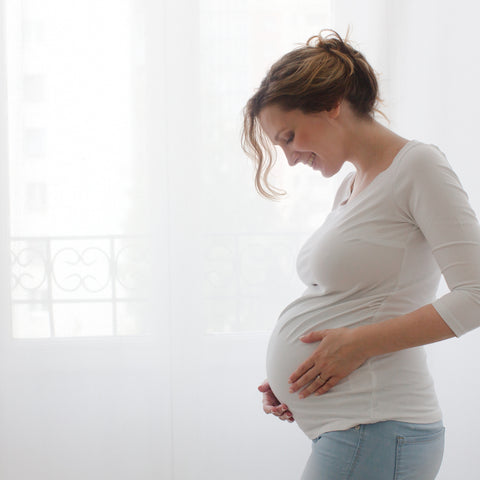 senhora grávida com as suas mãos segura na barriga e sorri