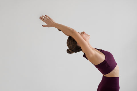 senhora jovem com o cabelo apanhado e roupas cor de vinho, a praticar yoga